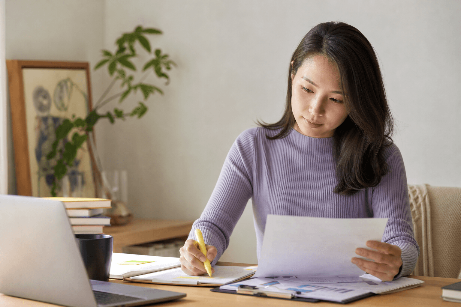 A woman reviews a printout with a highlighter beside her laptop.